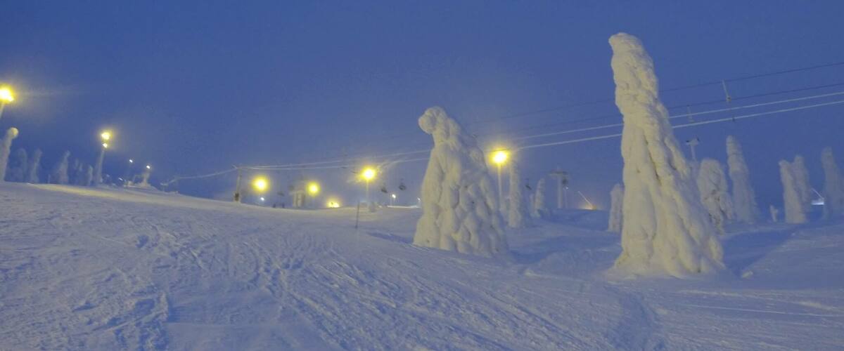 Eine mit Schnee bedeckte Skipiste bei Nacht, beleuchtet von künstlichem Licht.