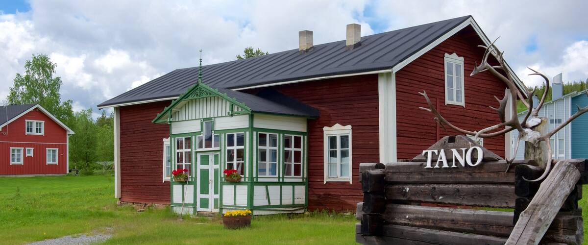 A red wooden house with a green porch and a sign that reads "TANO".