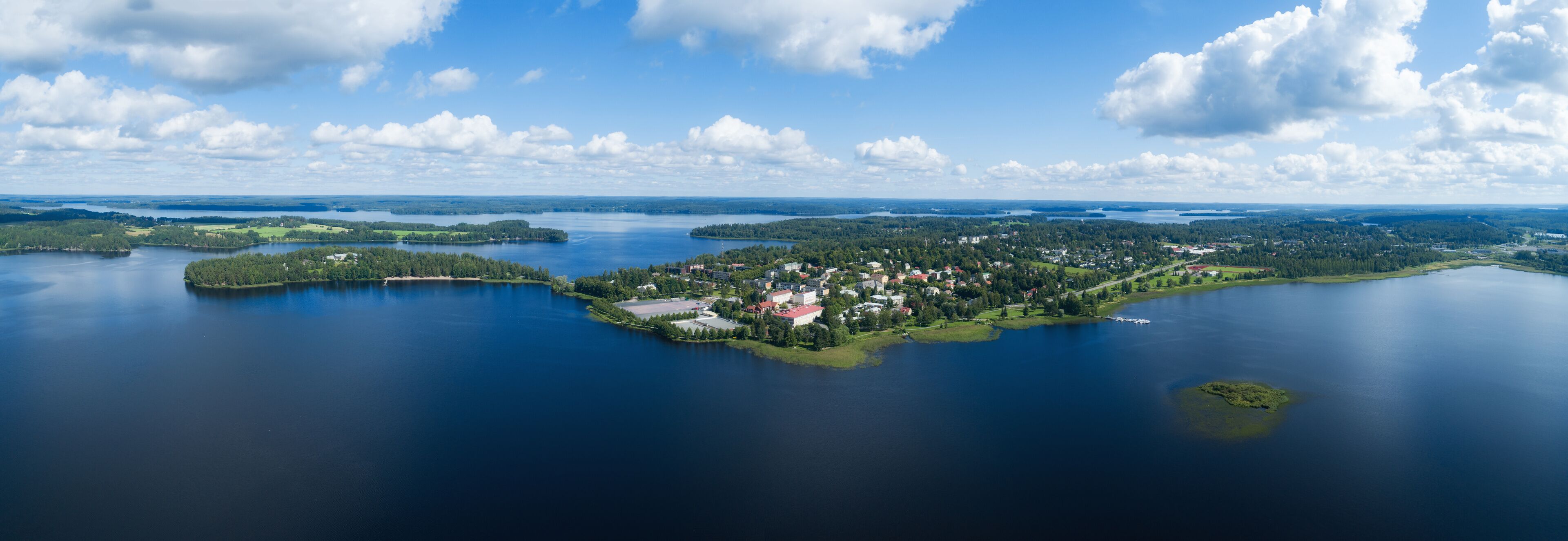 An aerial view of a lake surrounded by forested islands and a small town with red-roofed buildings.