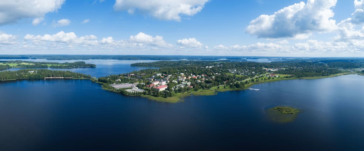 An aerial view of a lake surrounded by forested islands and a small town with red-roofed buildings.