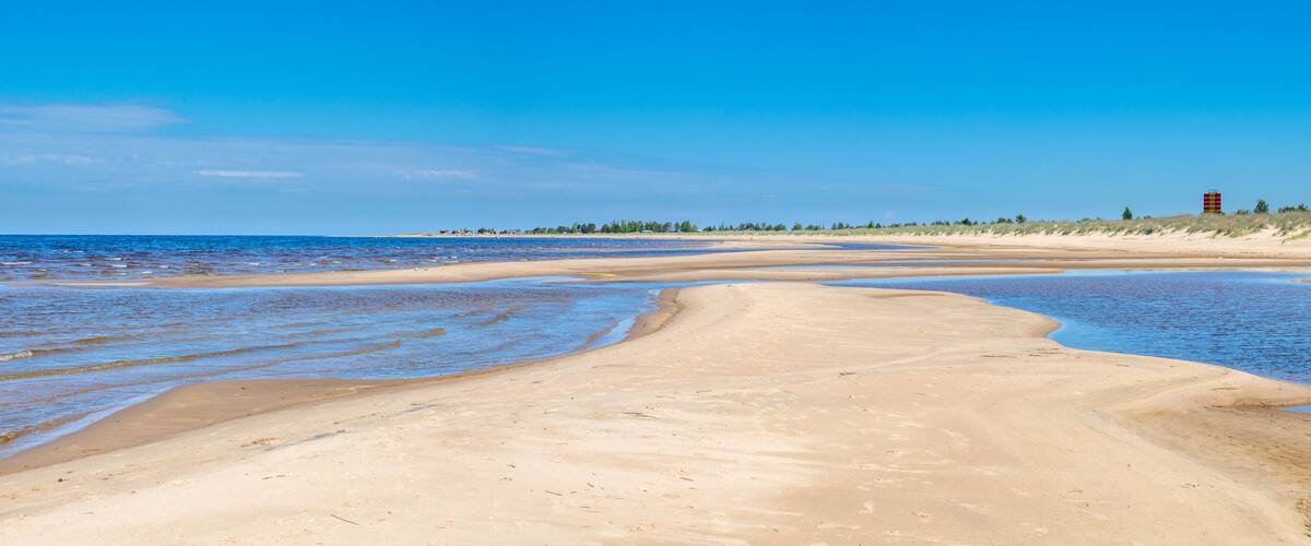 A sandy beach with gentle waves, a clear blue sky, and a lifeguard tower in the distance.