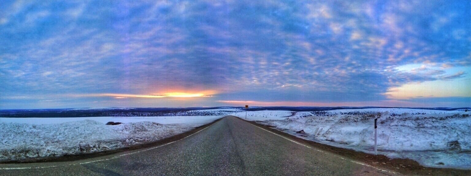 Uma estrada coberta de neve com o pôr do sol ao longe.