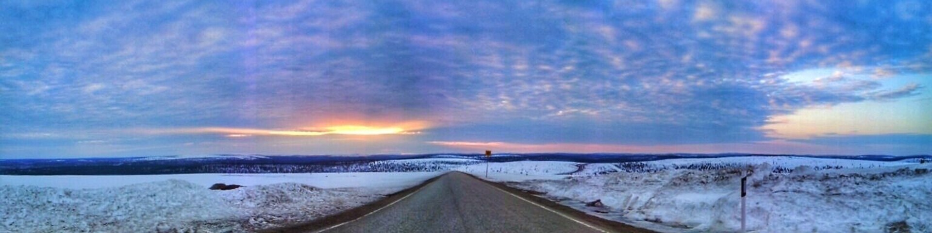 Uma estrada coberta de neve com o pôr do sol ao longe.