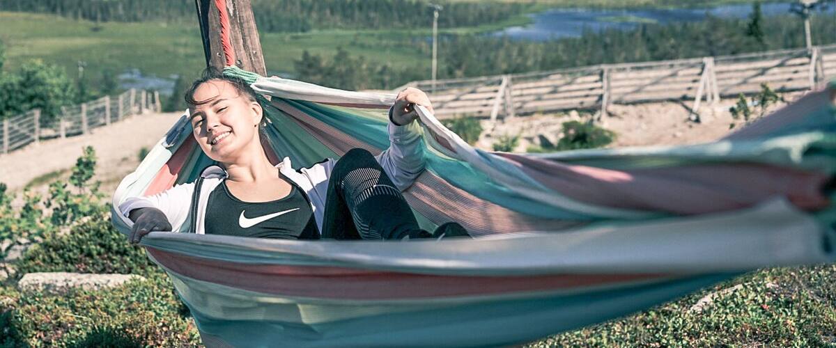 A person relaxing in a hammock with a scenic view of a forest and a lake in the background.