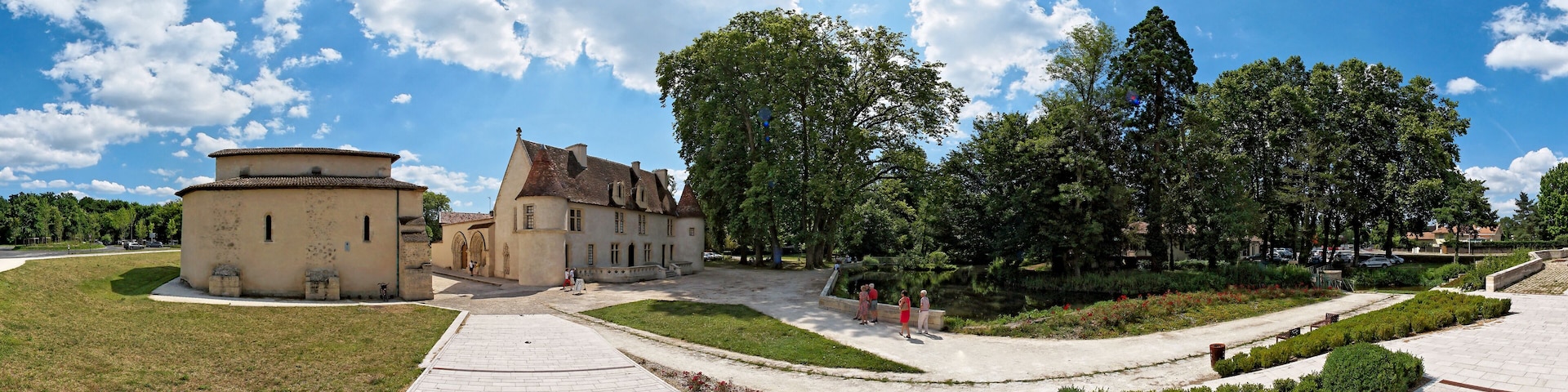 A historic building complex with a courtyard, surrounded by trees and a clear sky.