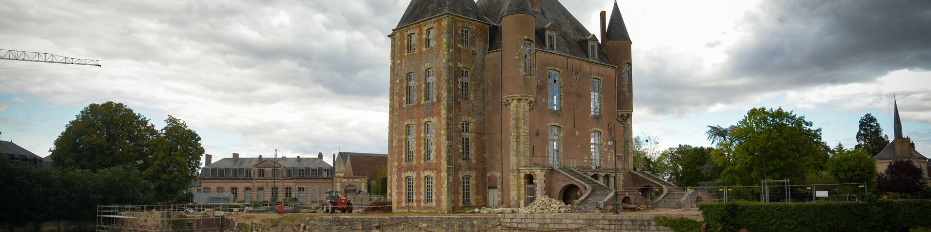 Un edificio histórico con una torre, rodeado de vegetación y un río.