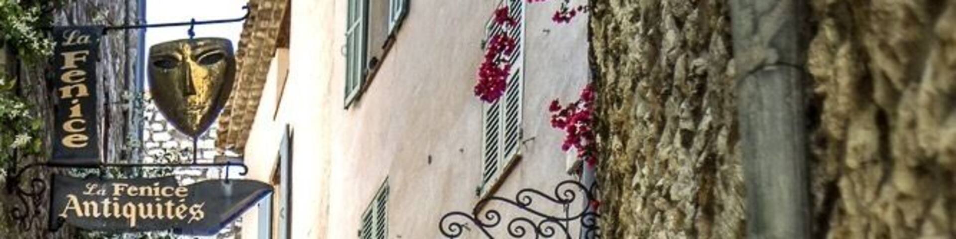 A narrow stone staircase leading up a hill, with orange flowers in pots along the path and a sign for 'La Fenice Antiques' above.