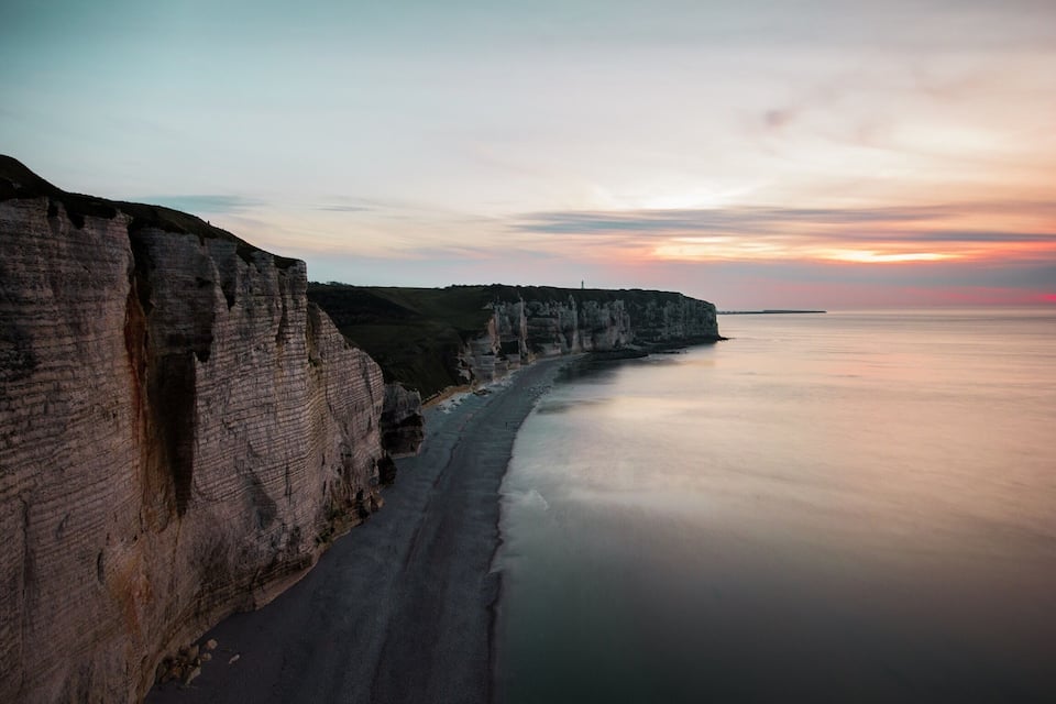 Une falaise côtière surplombant une longue plage étroite et une mer calme.