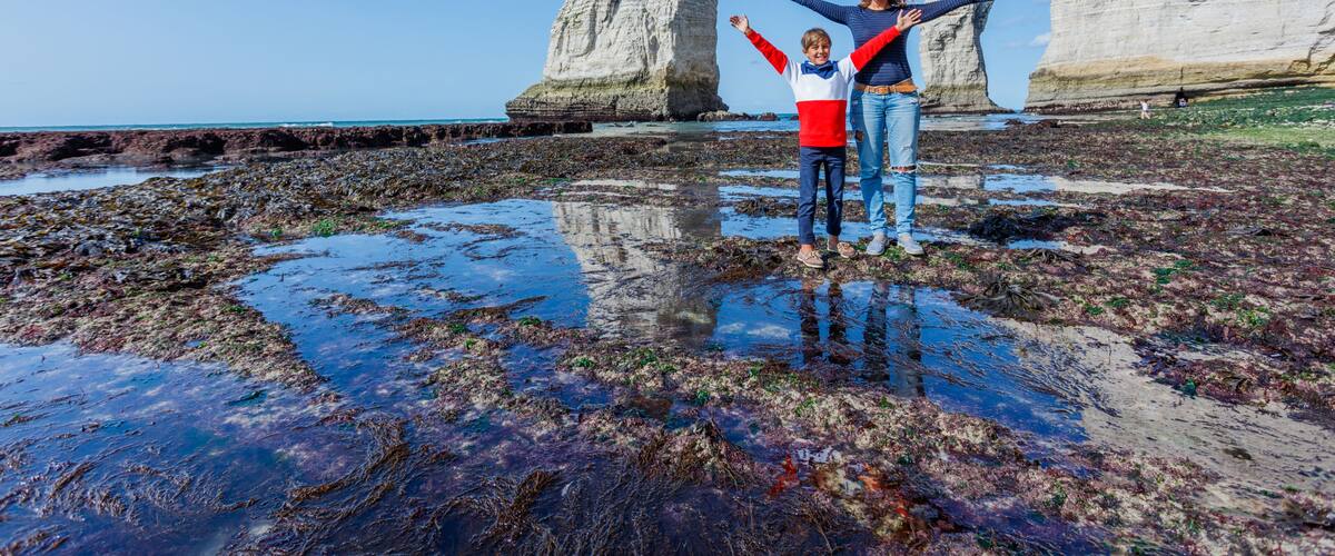 Two people standing on a tidal flat with white chalk cliffs in the background.