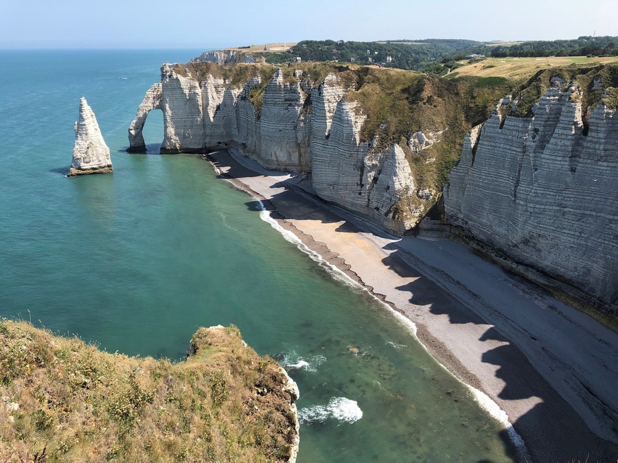 A coastal landscape with white cliffs, a clear blue sea, and a sandy beach.