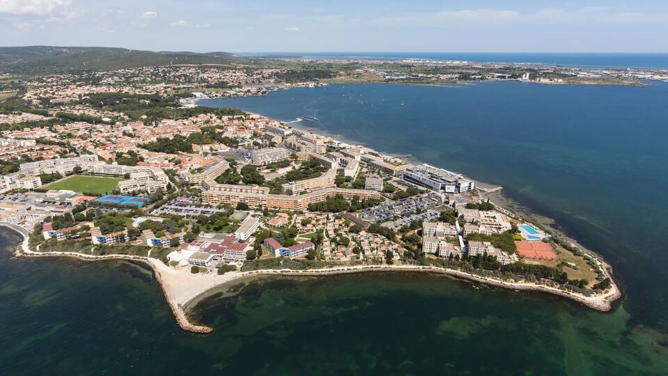 An aerial view of a coastal city with a prominent peninsula, dense urban areas, and a large body of water.