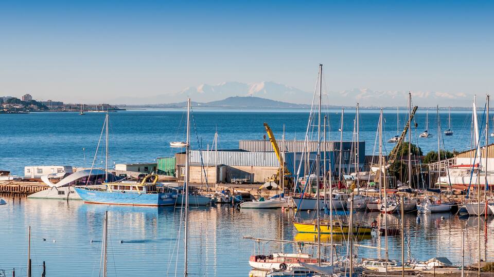 A marina with boats, a crane, and mountains in the background.