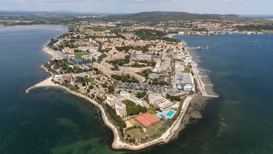 An aerial view of a coastal city with a prominent peninsula, clear blue waters, and a mix of residential and commercial buildings.