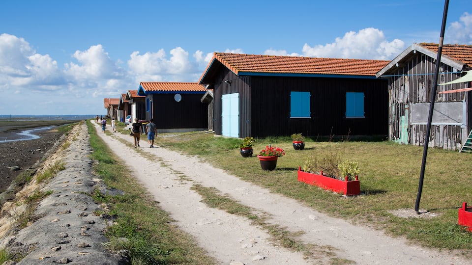 A coastal path with wooden houses, a beach, and a clear sky.