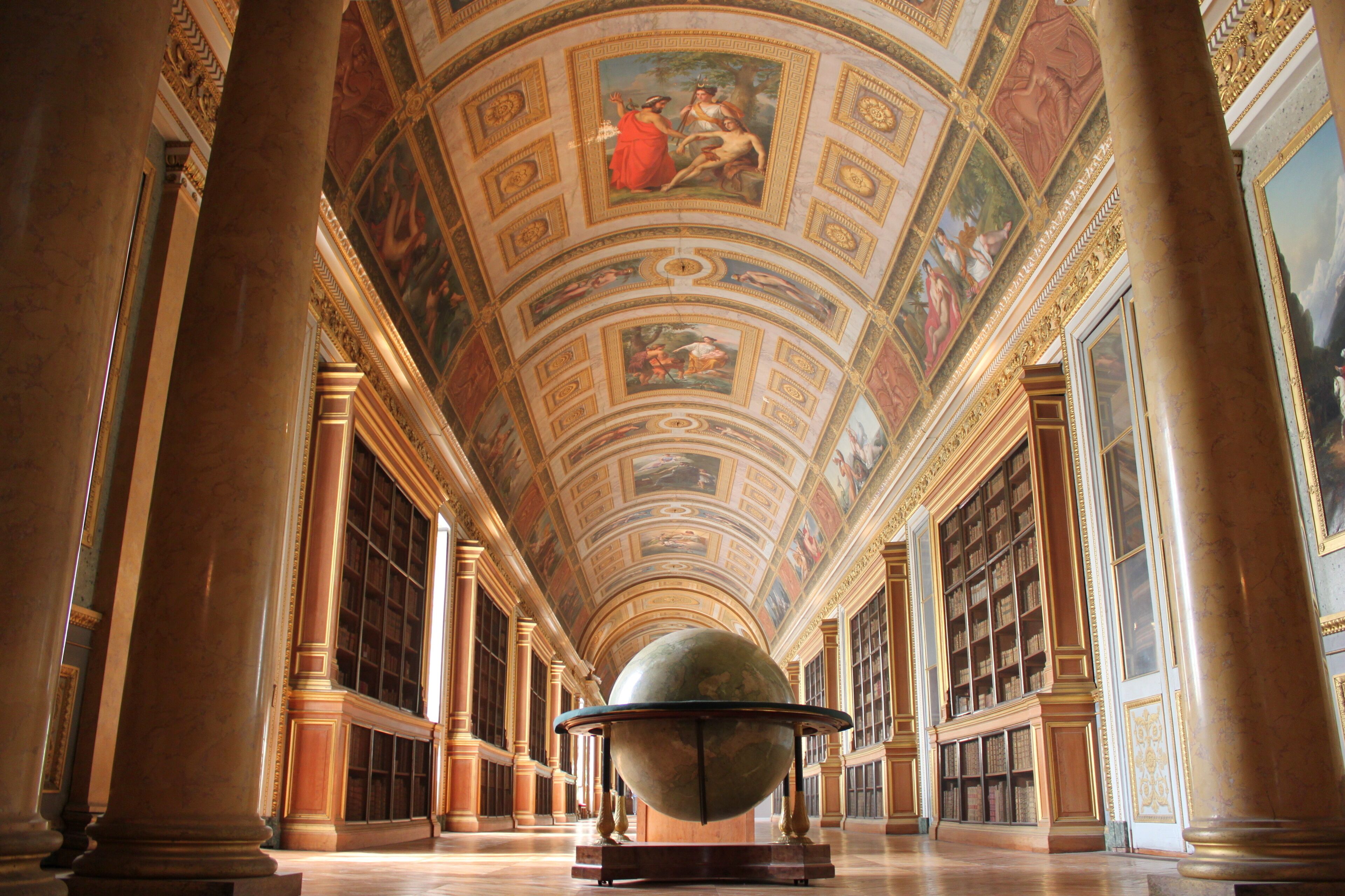 A grand hall with a large globe, ornate columns, and a high ceiling with frescoes.