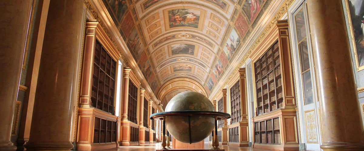 A grand hall with a large globe, ornate columns, and a high ceiling with frescoes.