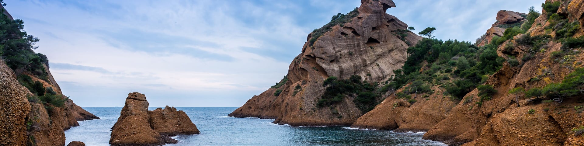 A coastal landscape with rocky cliffs, a calm sea, and a clear sky.