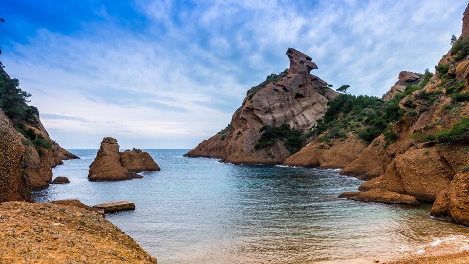 A coastal landscape with rocky cliffs, a calm sea, and a clear sky.