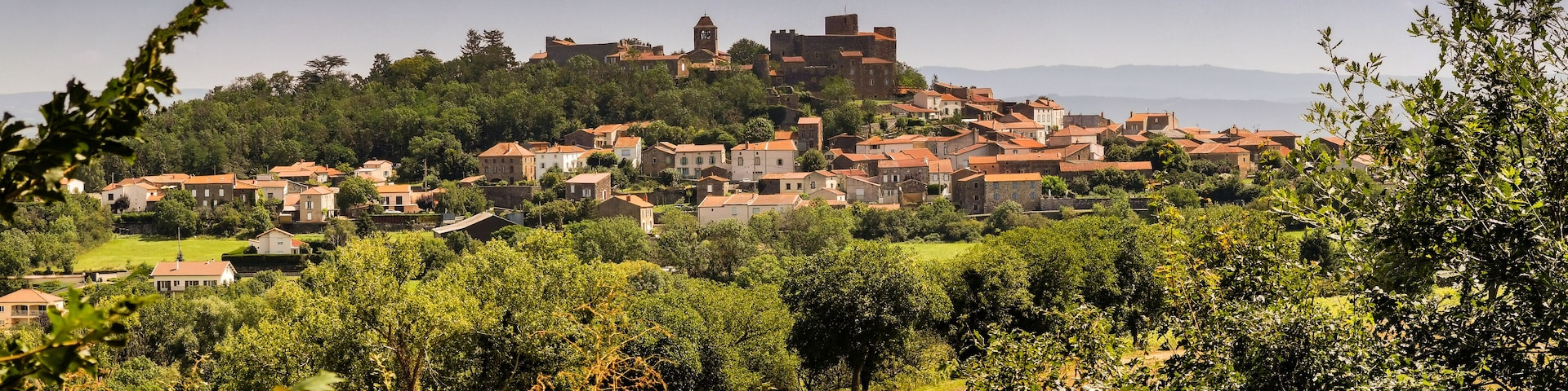 Uma aldeia numa encosta com edifícios tradicionais, um castelo e vegetação exuberante.