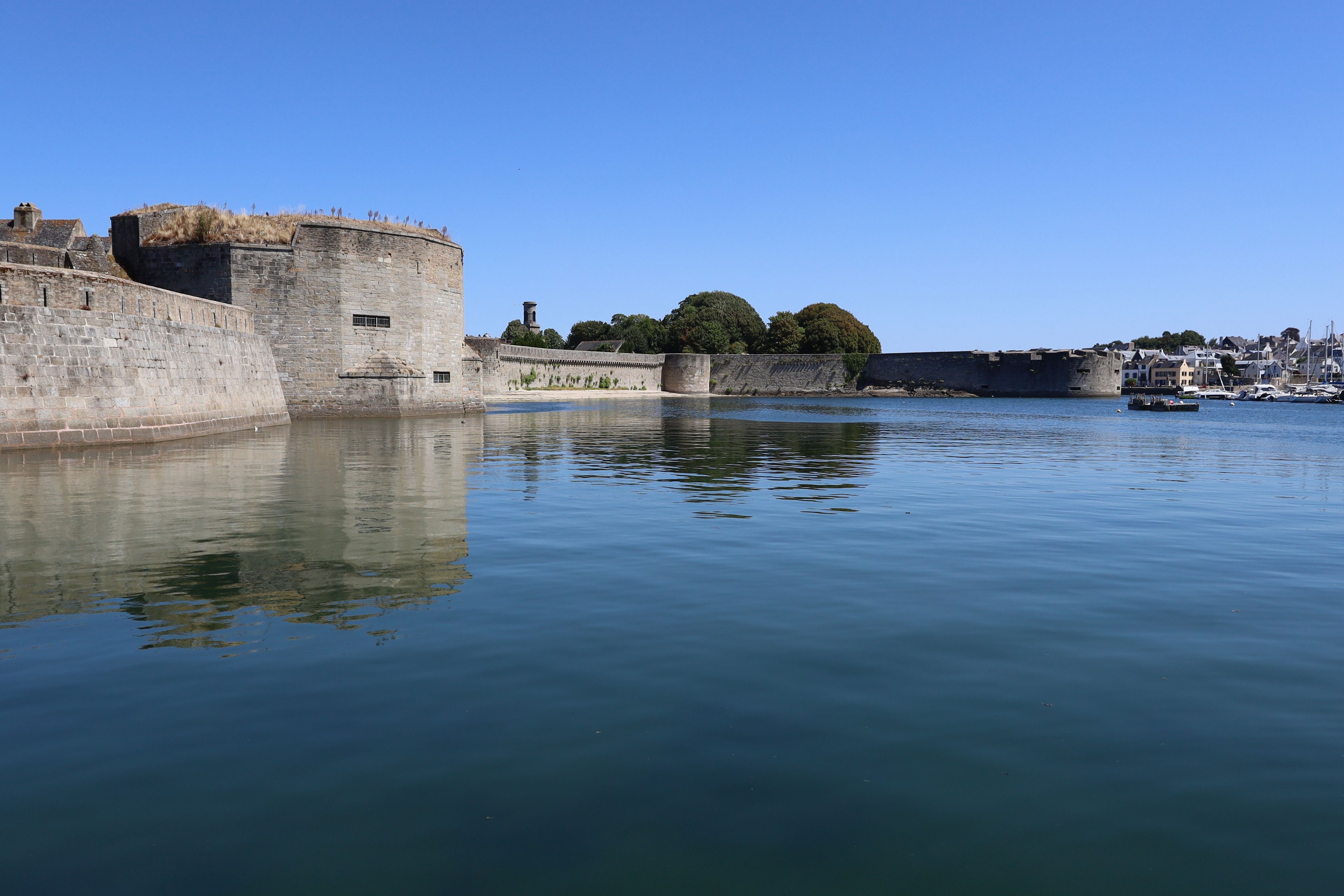 A historic stone fortification by a calm body of water with a clear sky.