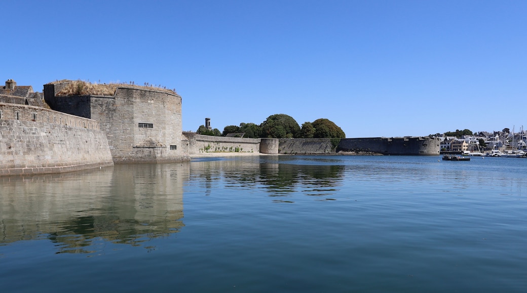 A historic stone fortification by a calm body of water with a clear sky.