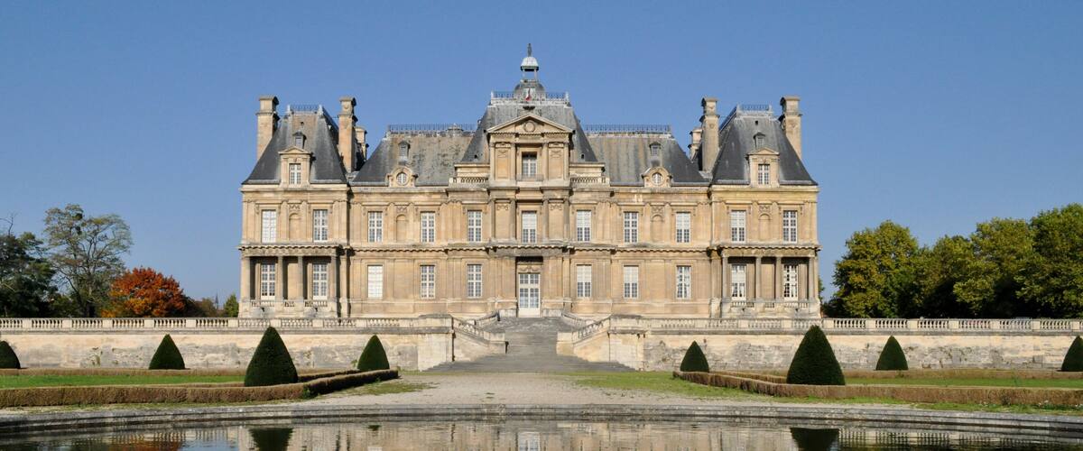 A large, historic building with a symmetrical facade, a central entrance, and a reflecting pool in front.