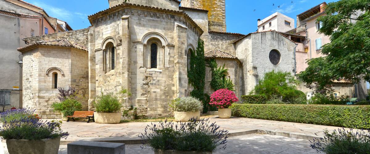 Un edificio histórico de piedra con un campanario, rodeado de plantas en macetas y un banco.