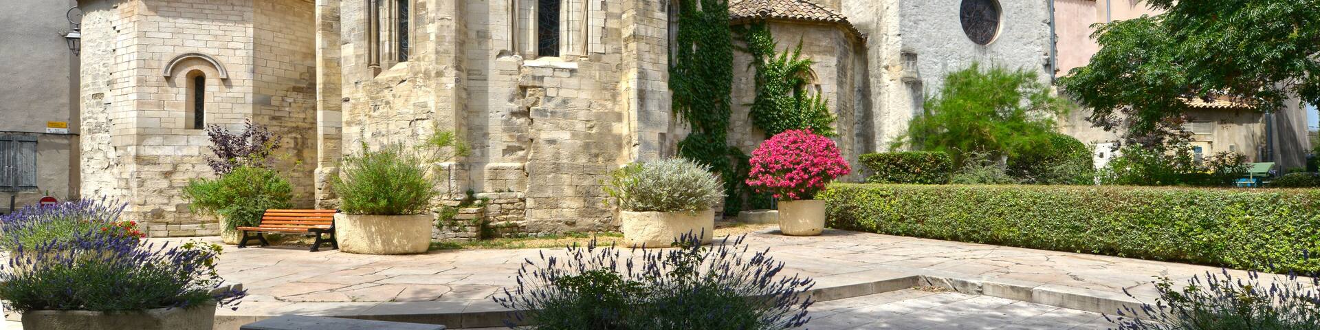 A historic stone building with a bell tower, surrounded by potted plants and a bench.
