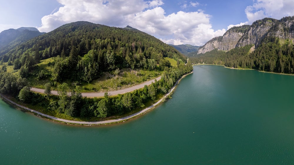Un lac entouré de montagnes boisées, avec une route sinueuse qui le longe.