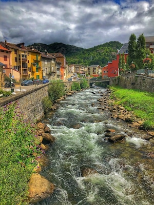 Um rio serpenteando por uma cidade com edifícios coloridos e montanhas ao fundo.