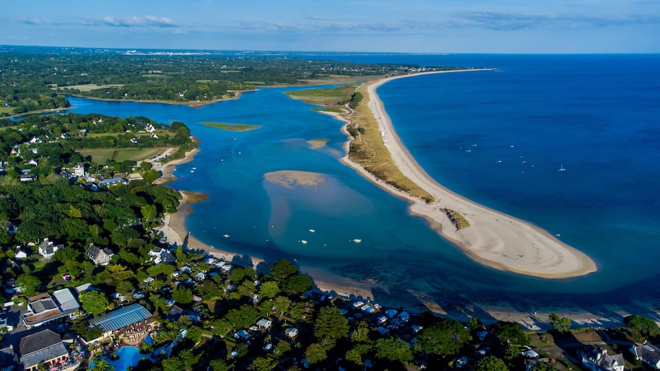 An aerial view of a coastal area with a large bay, a sandy beach, and a dense cluster of houses.