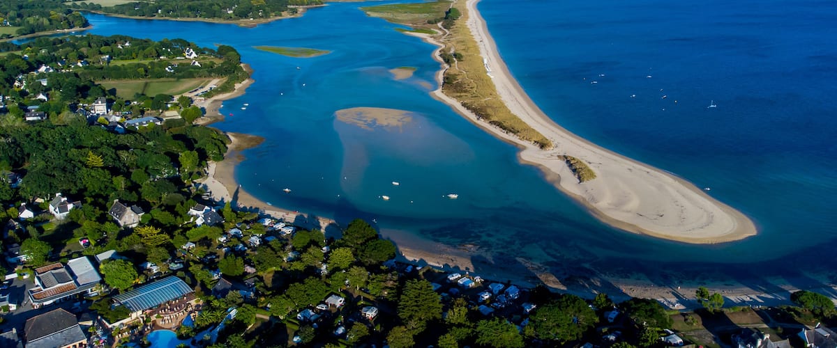An aerial view of a coastal area with a large bay, a sandy beach, and a dense cluster of houses.