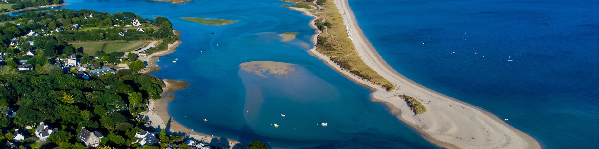 An aerial view of a coastal area with a large bay, a sandy beach, and a dense cluster of houses.