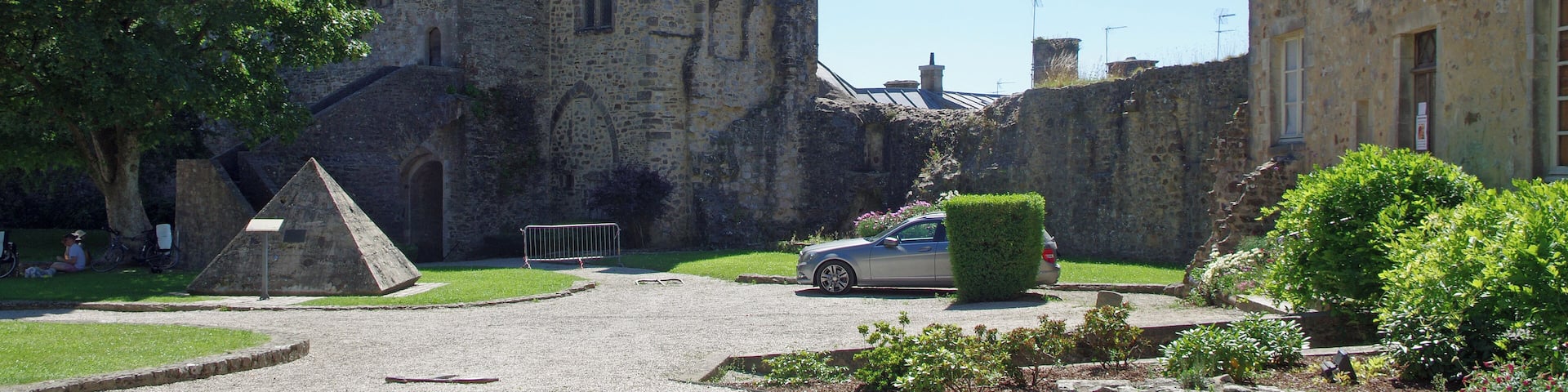 Bricquebec-en-Cotentin (Manche). Le château (La cour intérieur) La Tour de l'Horloge : Enorme tour rectangulaire avec son clocheton, c'est le châtelet d'entrée. La tour est percée de deux portes, une porte piétonne et une porte charretière. Le châtelet est construit en schiste pour la partie basse et en grès pour les étages. Les entourages de fenêtres sont en calcaire. On accède aux étages par un escalier externe côté cour. La Pyramide de mémoire : Pyramide création de l'architecte-designer Pascal Morabito pour célébrer le passage à l'an 2000. La Pyramide de mémoire contient 2000 objets du souvenir dons des Bricquebétais, douilles, briquets, casques, éclats d'obus, etc. Ces objets sont emprisonnés dans un mortie composé avec du sable des plages du débarquement de la Seconde Guerre mondiale. L'érosion laissera réapparaître les objets aux générations futures. Une partie du chartrier : Bâtiment où étaient conservés les chartes, les titres prouvant les droits seigneuriaux.
