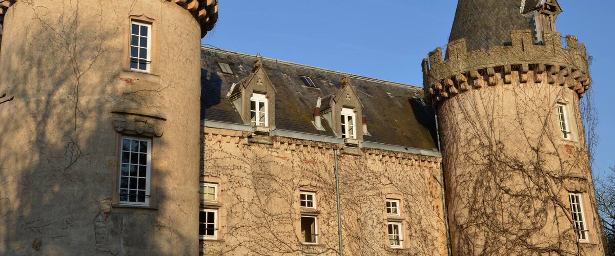 A historic castle with two prominent towers, ivy-covered walls, and multiple windows.