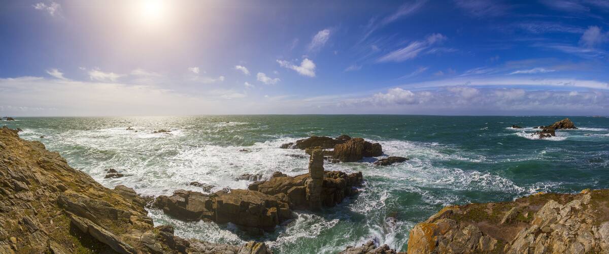 A rocky coastline with waves crashing against the rocks under a clear sky.