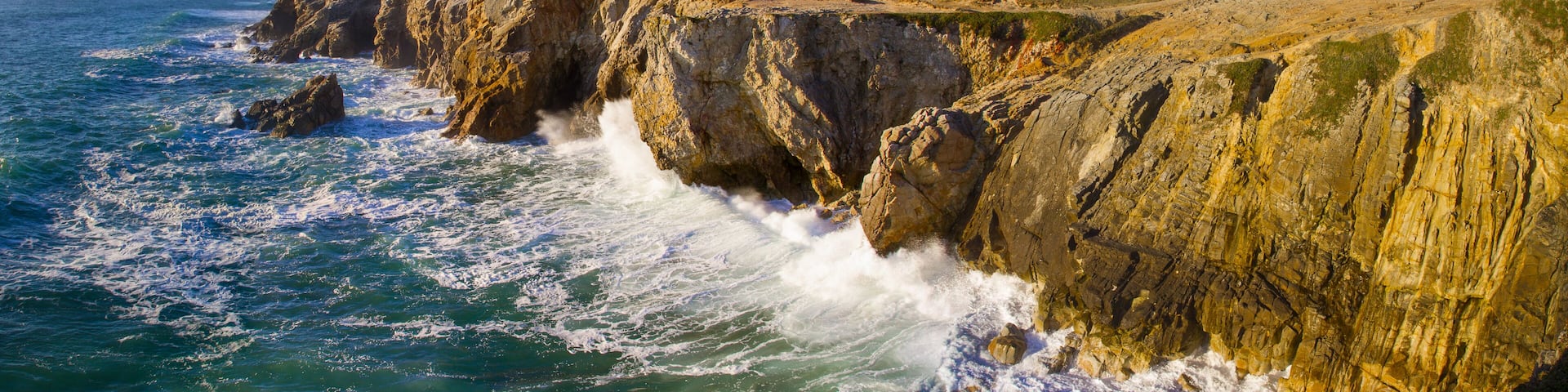 A coastal cliff with waves crashing against it.