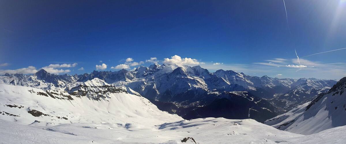 A snow-covered mountain range with a clear blue sky and a visible contrail.