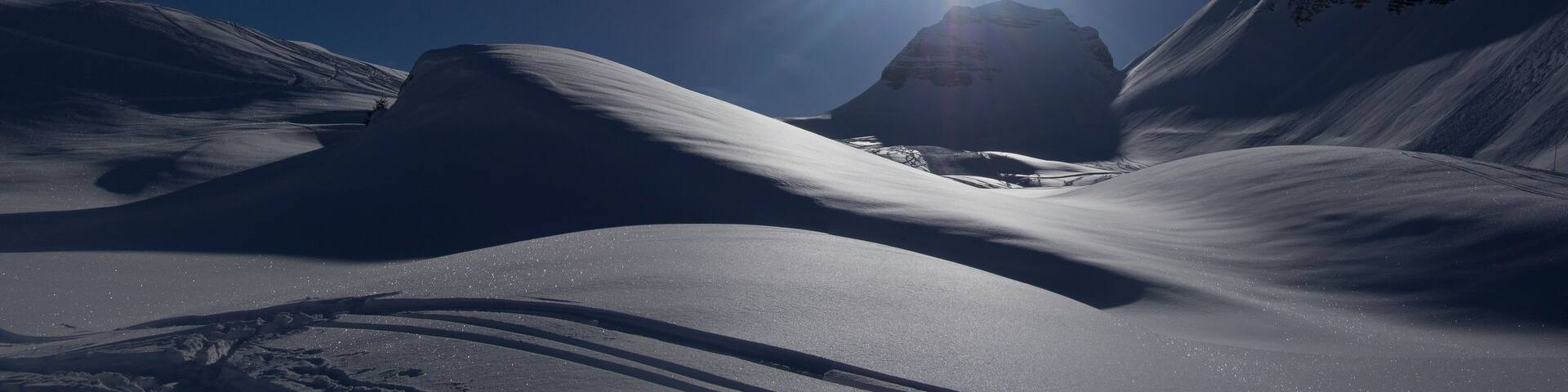 A snow-covered mountain landscape with a bright sun in the background.
