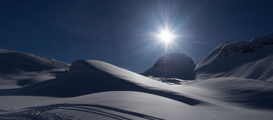 Un paisaje montañoso cubierto de nieve con un sol brillante al fondo.