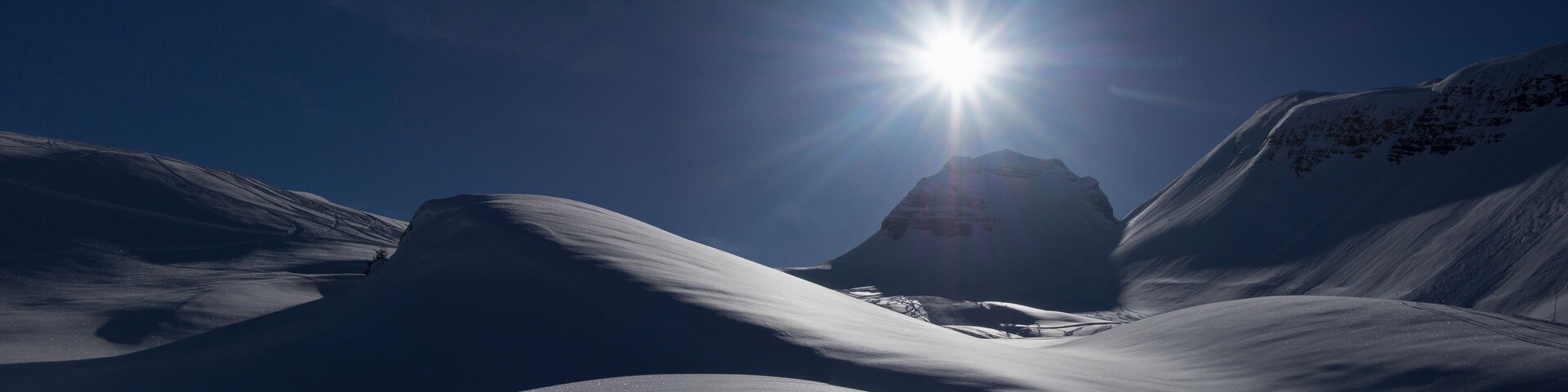 Un paisaje montañoso cubierto de nieve con un sol brillante al fondo.
