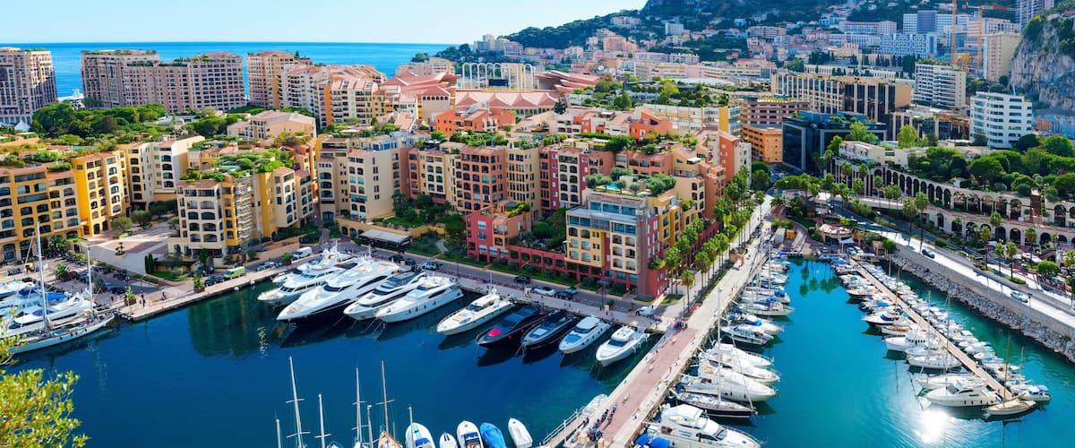 A marina with numerous yachts docked, surrounded by colorful buildings and a coastal cityscape.