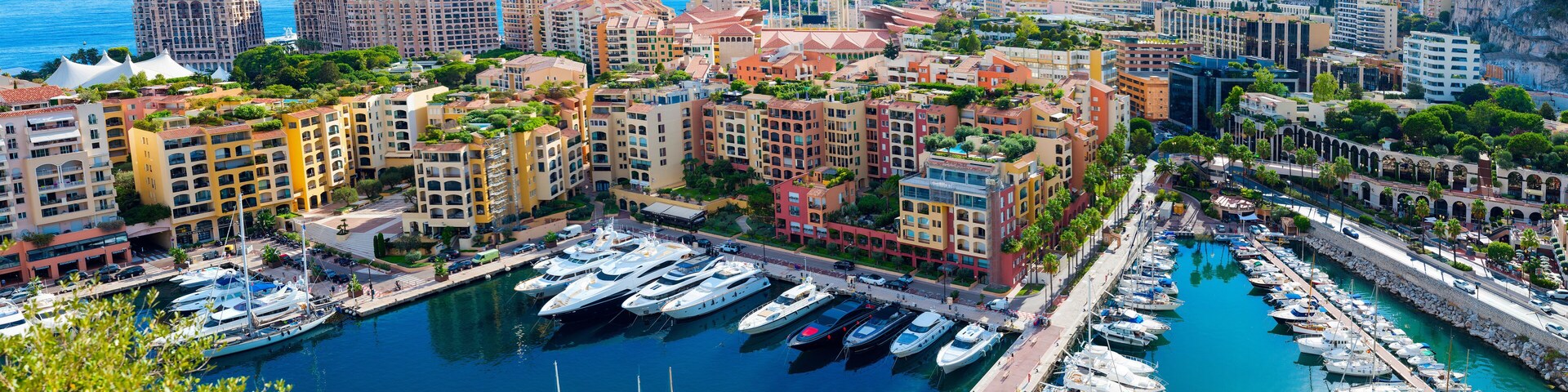 A marina with numerous yachts docked, surrounded by colorful buildings and a coastal cityscape.