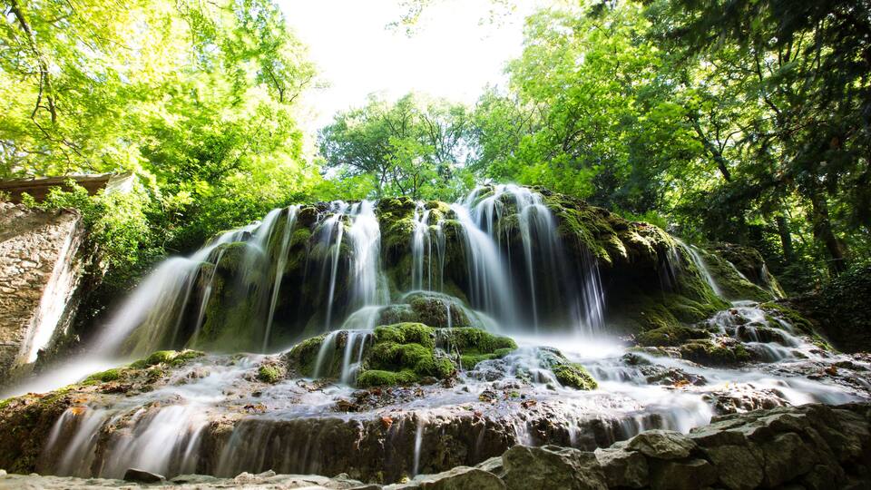 A multi-tiered waterfall surrounded by lush green foliage.