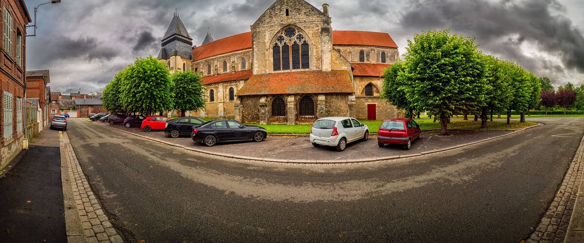 A church with a red roof and a tall tower, surrounded by parked cars and trees.
