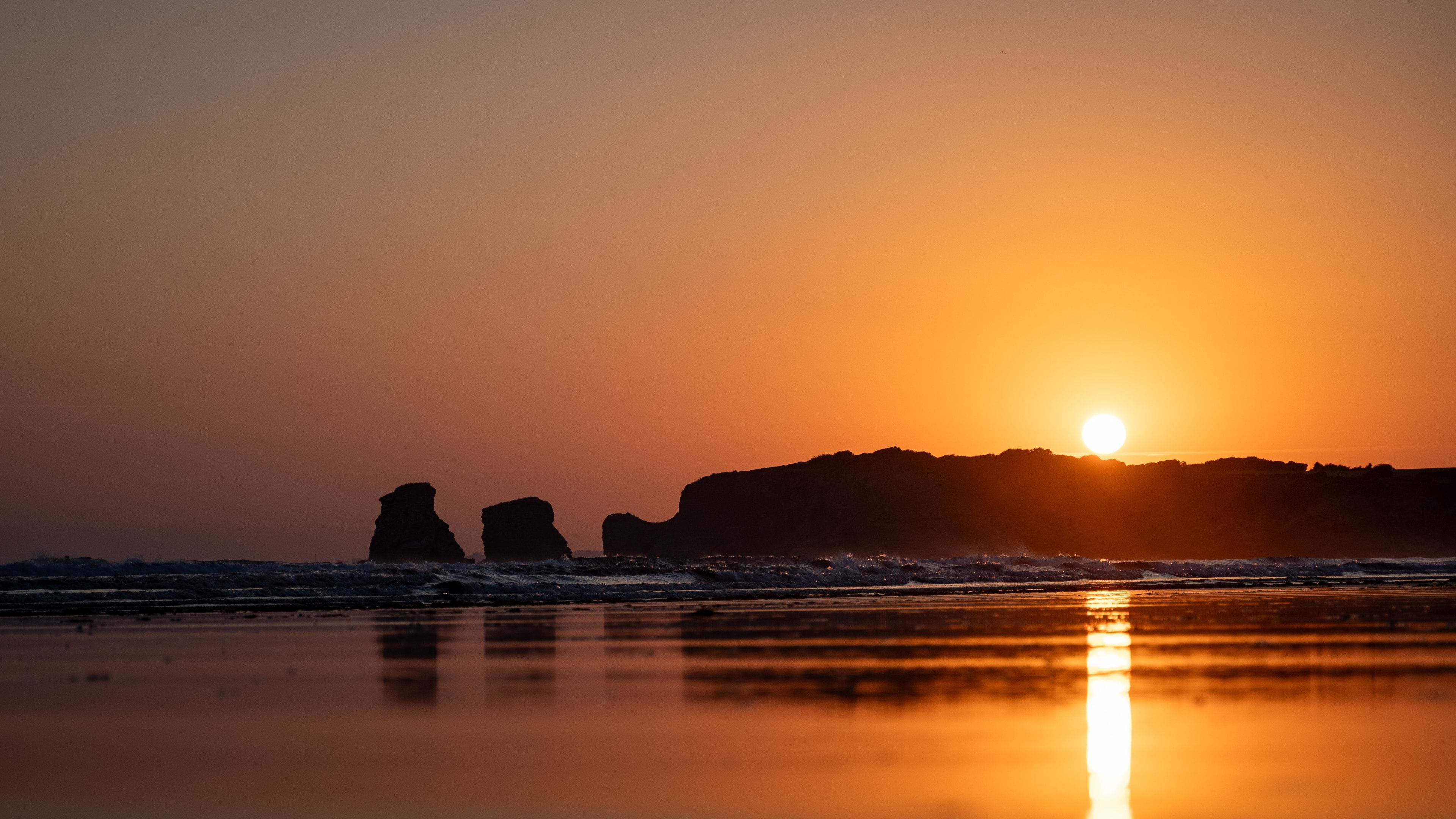Ein Sonnenuntergang über einem Strand mit gegen den Himmel abgesetzten Felsformationen.