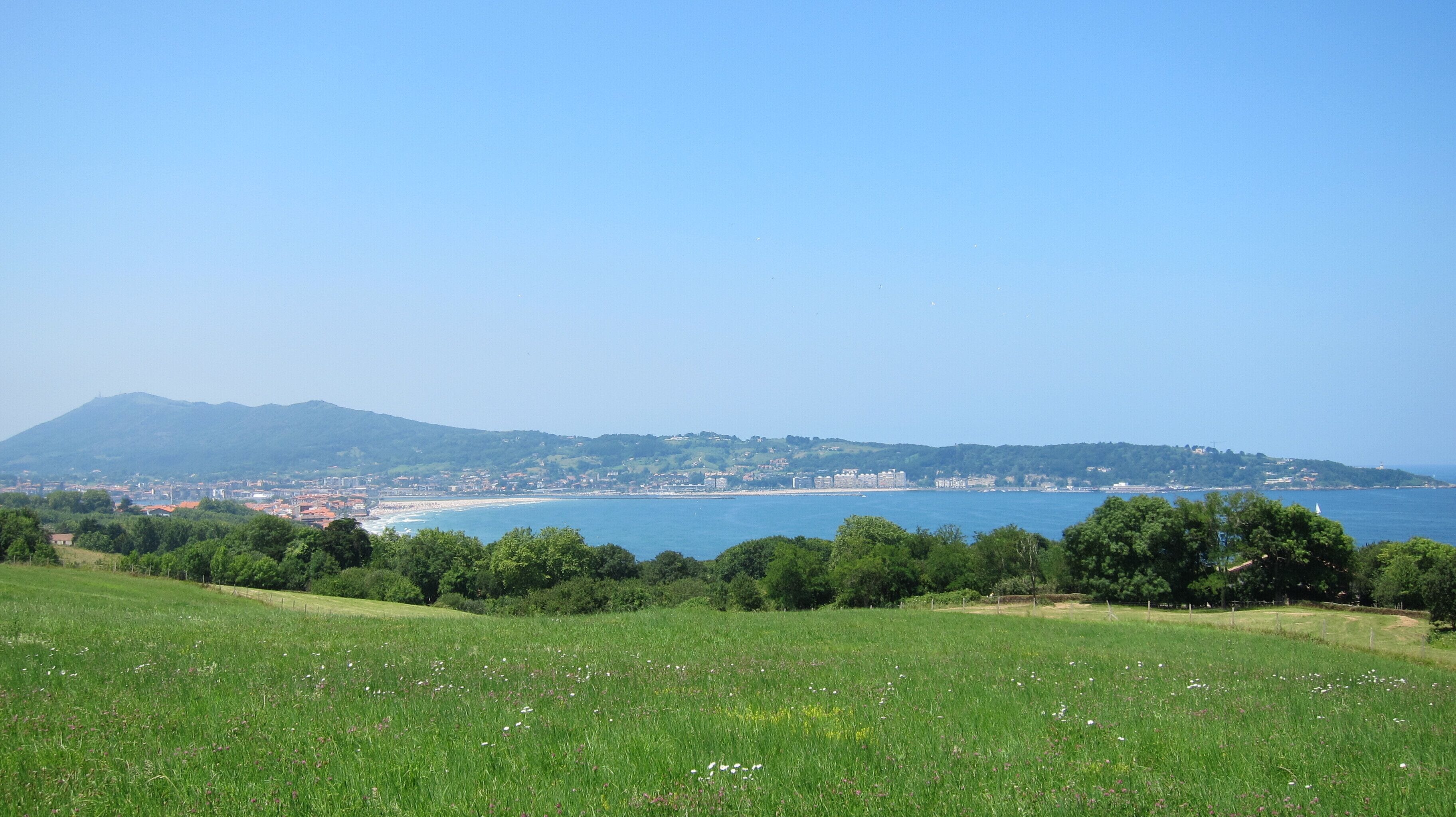 A coastal landscape with a beach, a city in the distance, and a mountain range.