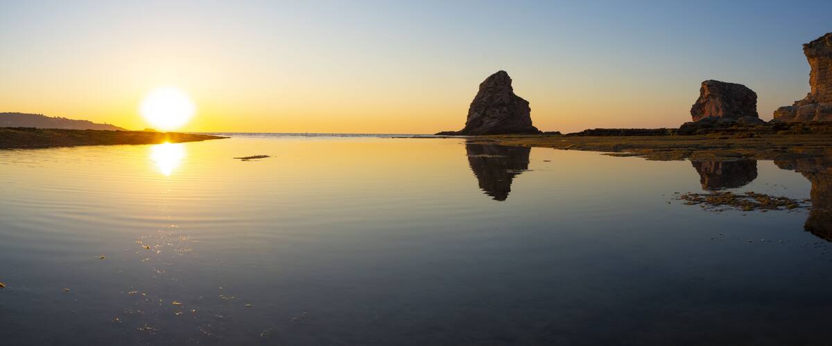 A sunset over a calm lake with rock formations.
