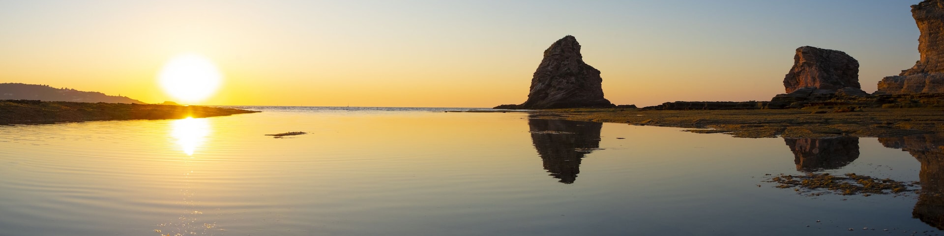 A sunset over a calm lake with rock formations.