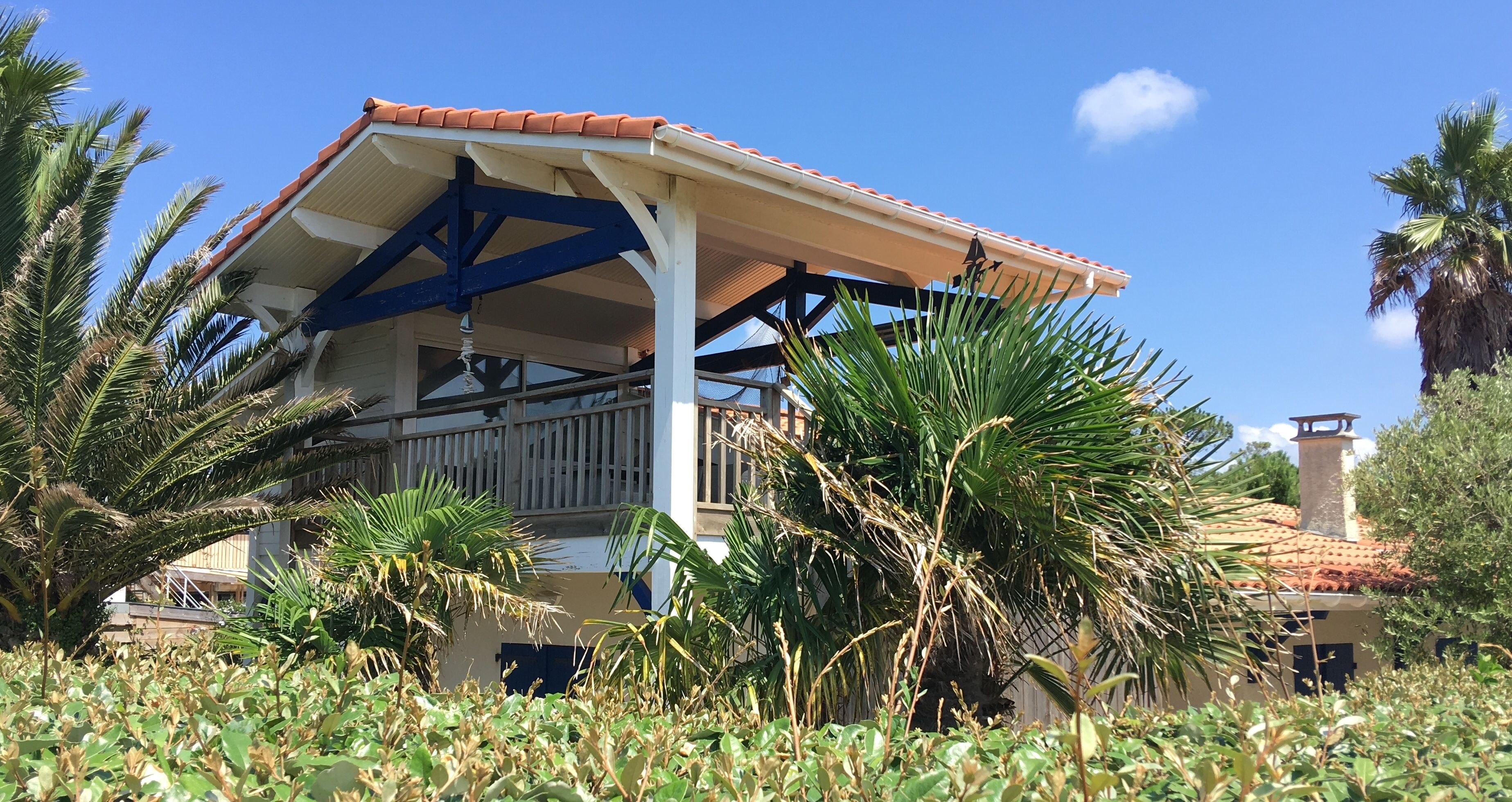 A covered outdoor area with a tiled roof, surrounded by palm trees and vegetation.